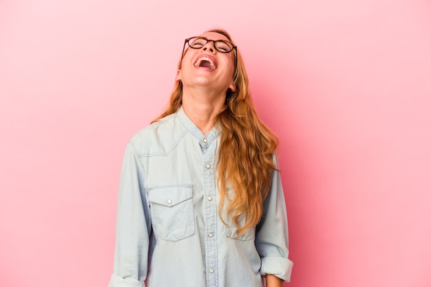 Caucasian blonde woman isolated on pink background relaxed and happy laughing, neck stretched showing teeth.