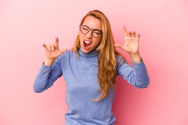 Caucasian blonde woman isolated on pink background showing claws imitating a cat, aggressive gesture.