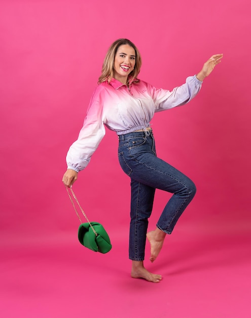 Caucasian blonde woman smiling with a green bag on a pink background full length shot