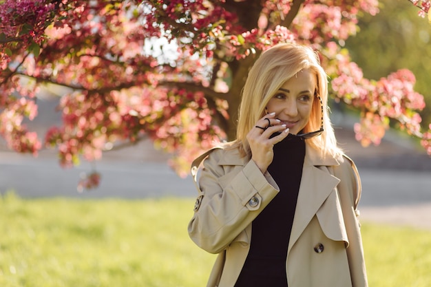 Caucasian blonde woman wearind trench smile happily on sunny spring day outside walking in park