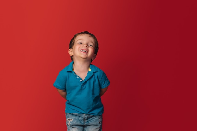 Caucasian blondie boy laughing in a blue t-shirt on a red background. copy space.