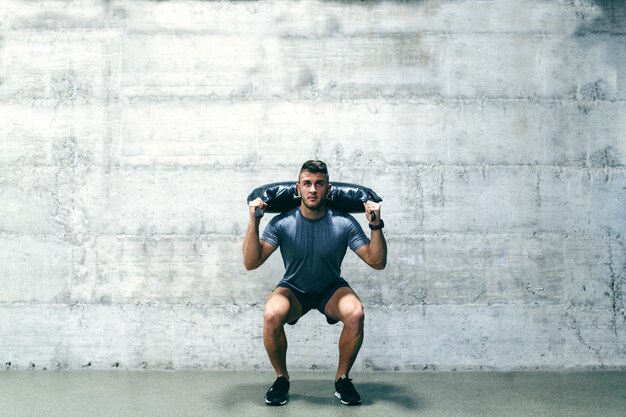 Caucasian bodybuilder with serious facial expression working out with Bulgarian Training bag.