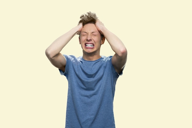 Foto il ragazzo caucasico sta avendo un esaurimento nervoso. un bel ragazzo vestito casual si sta tirando i capelli per la disperazione. isolato su sfondo bianco.