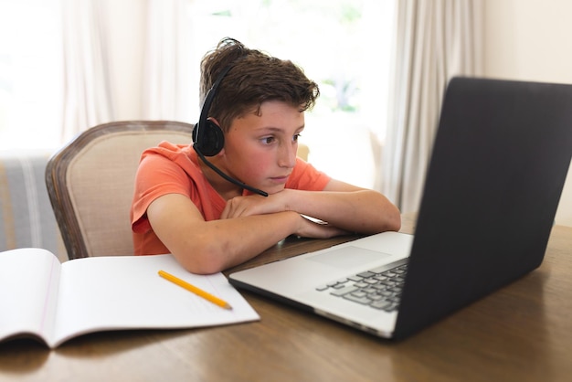 Caucasian boy learning and using laptop and headphones siting in living room