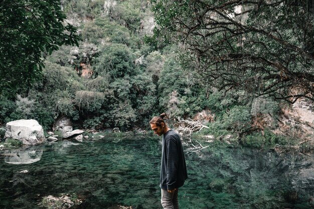 Photo caucasian boy looking at the ground standing calm and relaxed by the water of the small transparent