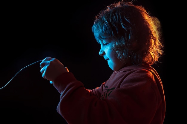 Портрет кавказского мальчика, изолированные на темном фоне студии в неоновом свете