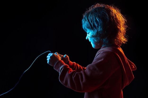 Caucasian boy's portrait isolated on dark studio background in neon light