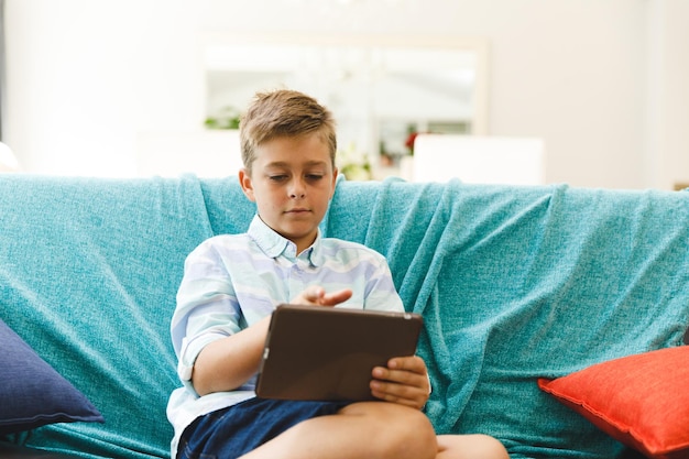 Photo caucasian boy sitting on couch and using tablet in living room