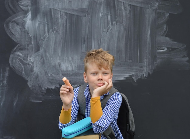 Caucasian boy sitting with chalk in hand Against a blackboard thinking Back to school