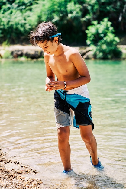 Caucasian boy in swimming trunks and diving goggles looking down into the river water in summer