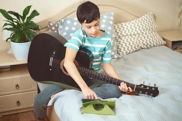 Caucasian boy teenager study playing acoustic guitar at home\
bedroom guitar lessons on internet and online music education\
concept