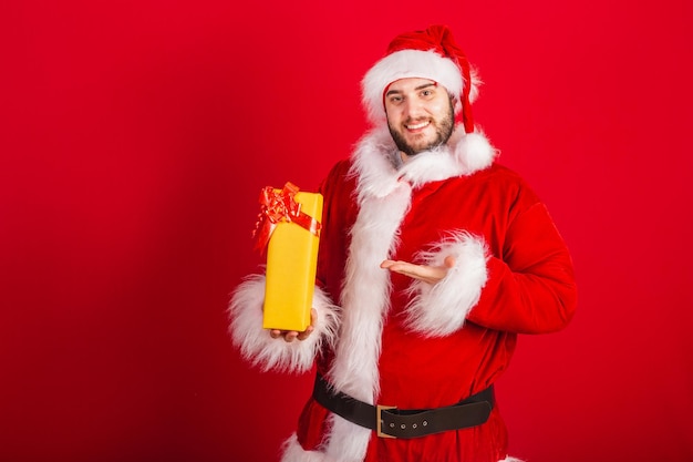 Caucasian brazilian man dressed in christmas outfit santa claus holding yellow gift