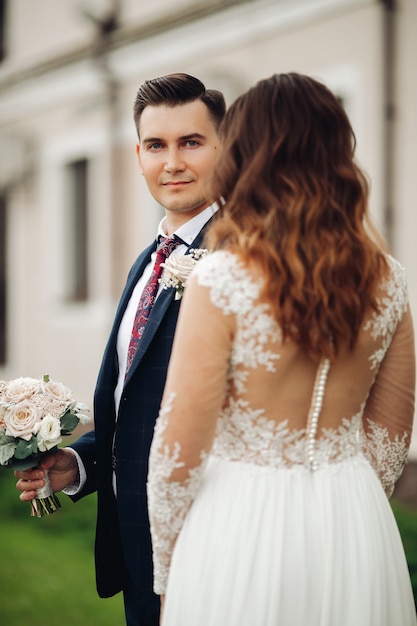 Caucasian bride with long wavy hair in long white dress sees to her strong husband