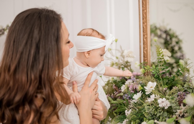 Caucasian brunette mom holds her baby daughter and sniffs flowers