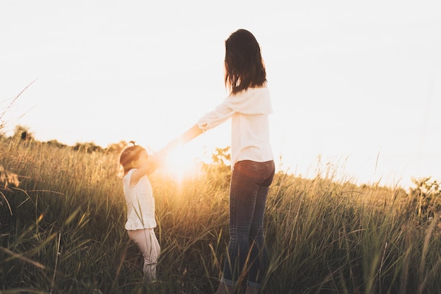 Caucasian brunette mother and child daughter playing on meadow sunset Beautiful brunette woman dance with her toddler girl on meadow sunset background Happy motherhood and childhood