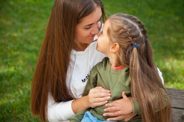 Caucasian brunette smiling woman looking at her daughter outside. Upbringing concept.