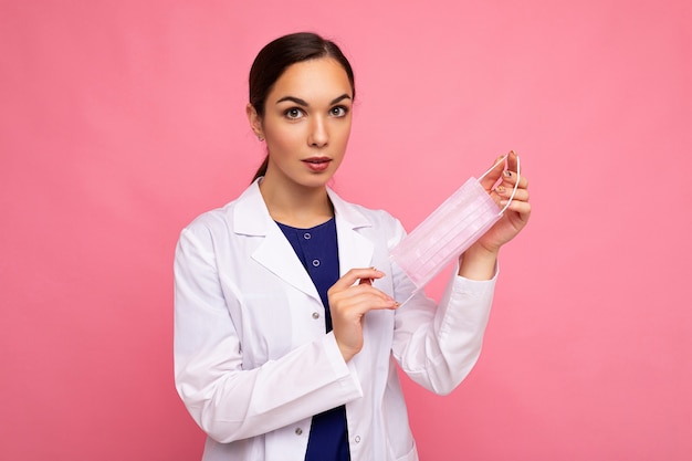 Caucasian brunette woman showing protection face mask isolated on pink