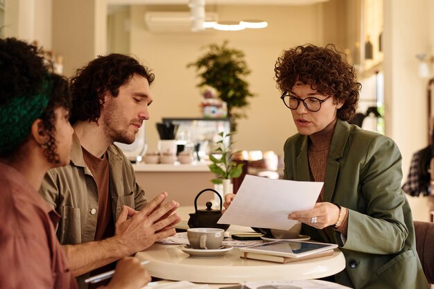 Photo caucasian business lady explaining in details information in documents to two young biracial people