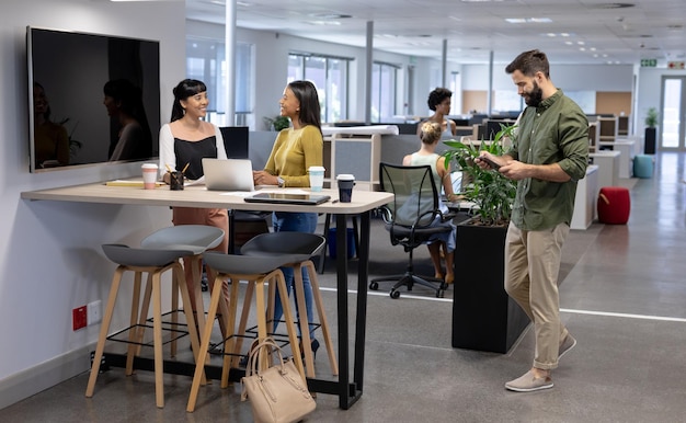 Caucasian businessman walking towards biracial businesswomen discussing during meeting in workplace