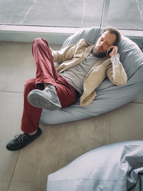 Caucasian businessman with a beard waiting for his flight at the airport and talking on the phone lying down