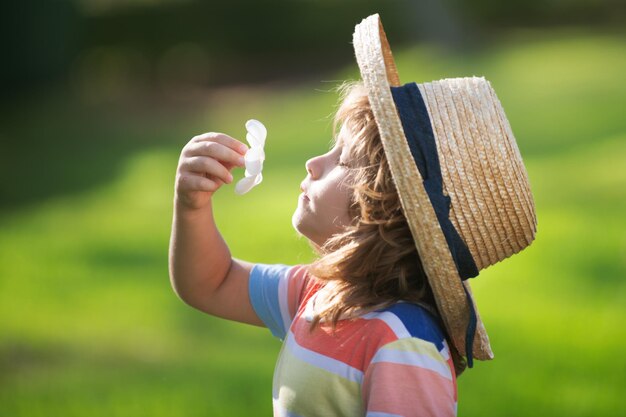 Caucasian child portrait close up kids in straw hat smelling plumeria flower on summer nature park