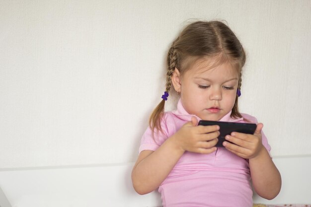 Caucasian child of three age holding mobile phone and looking on it on the white background