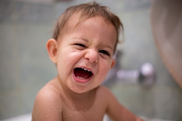 Photo caucasian child with sly smile opening his mouth and looking at camera the baby is wet bathes