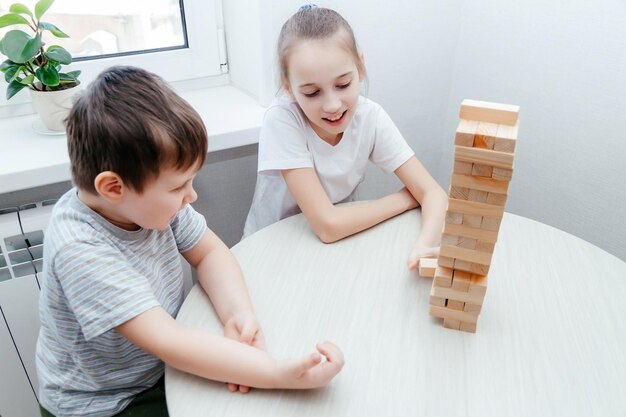 Caucasian children boy and girl playing jenga and smiling Block stacking game Home family activity party board offline game concept while staying at home during quarantine