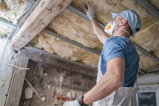 Photo caucasian contractor worker in his 30s replacing old attic mineral wool insulation wearing safe breath pro mask industrial home improvement and insulation materials theme