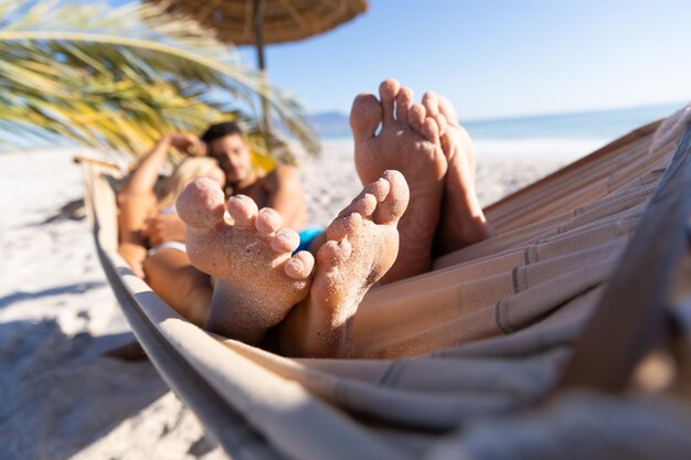 Caucasian couple enjoying time at the beach, lying on a hammock, embracing and holding hands