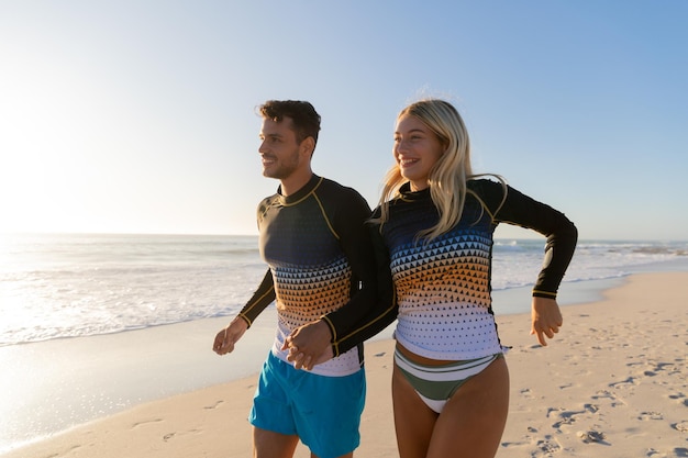 Caucasian couple enjoying time at the beach on a sunny day, walking and holding hands with sea in the background