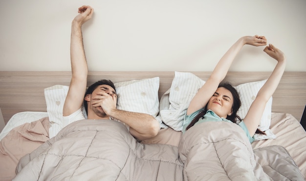 Caucasian couple getting up in the morning stretching arms and yawning