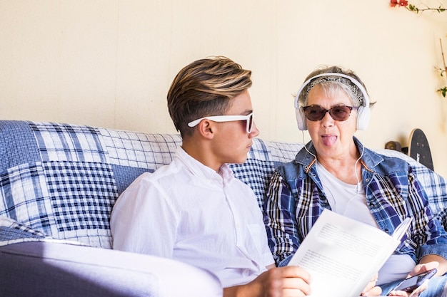 Caucasian couple grandmother and grandson study together and listne music or lesson with earphone the woman do funny crazy expression to the teenager that seriousle go on reading the book