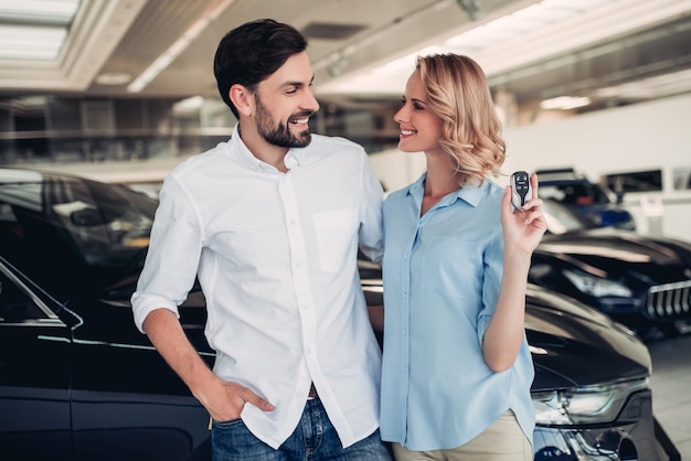 Caucasian couple holding keys of new car in dealership salon