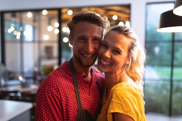 Caucasian couple at home together, standing in a kitchen, looking at the camera and smiling, social distancing and self isolation in quarantine lockdown during coronavirus covid19 epidemic