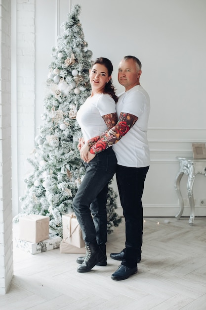 Caucasian couple in love hugs and smiles together near the christmas tree at home