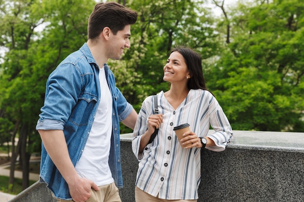 caucasian couple man and woman with paper cup smiling and talking while standing on stairs outdoors