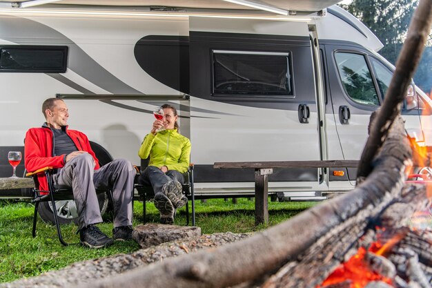 Photo caucasian couple in their 40s drinking wine in front of their modern rv camper van campsite family fun rving theme