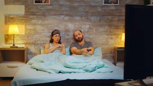 Caucasian couple using tv remote control at night. woman with\
sleep mask.