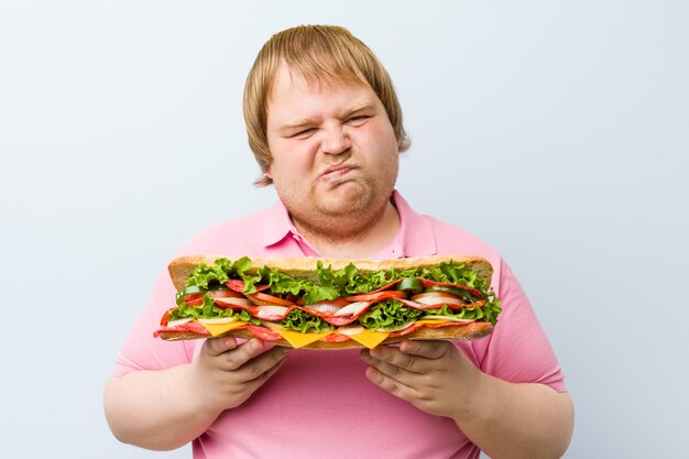 Кавказский сумасшедший блондин толстый мужчина держит гигантский бутерброд