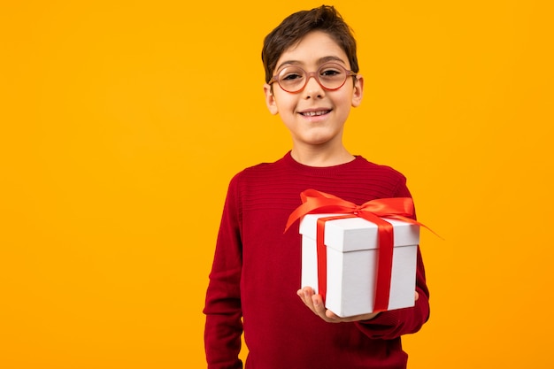 Caucasian cute boy in a red jumper with a gift box on yellow with copy space