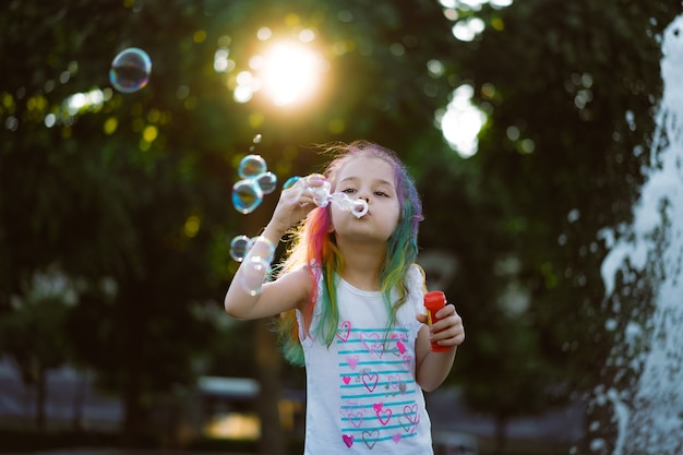 Кавказская милая маленькая девочка дует мыльные пузыри в парке