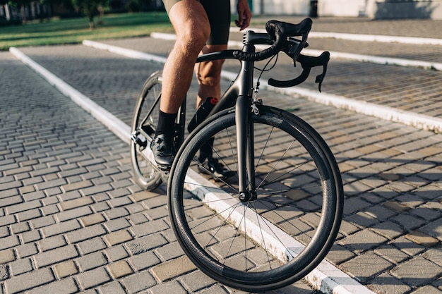 Caucasian cyclist in sport shoes and clothes sitting on black bike on fresh air Sportsman resting after riding outdoors Recreation and people concept