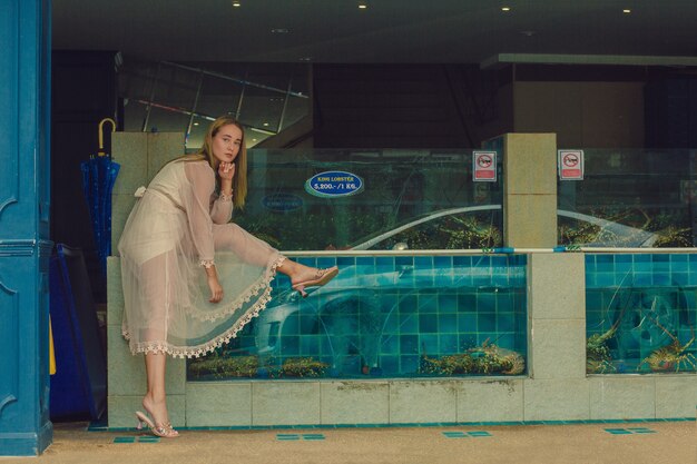 タイ、パタヤのキングロブスターと水族館の近くの透明なシフォンクリームのドレスでポーズをとる白人のダークブロンドのモデル。