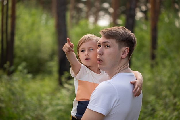 Caucasian daughter in daddys arms points a finger to the side in the forest