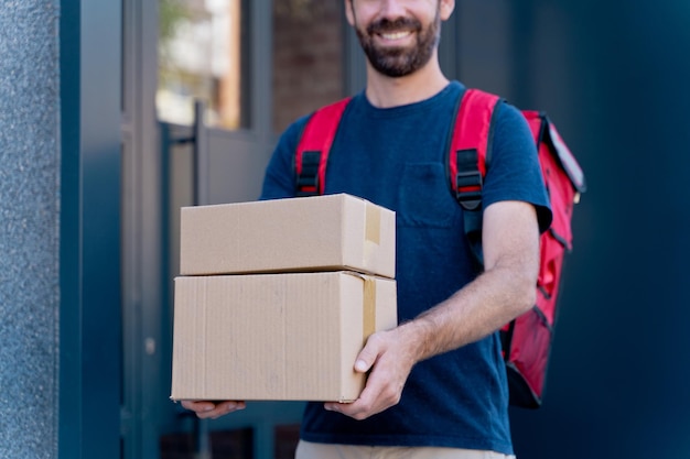 パーセルボックスを配達する白人配達人。宅配便のコンセプト。家に荷物を届ける幸せなライダーの水平方向のビュー。