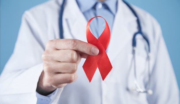 Caucasian doctor holds a red ribbon.