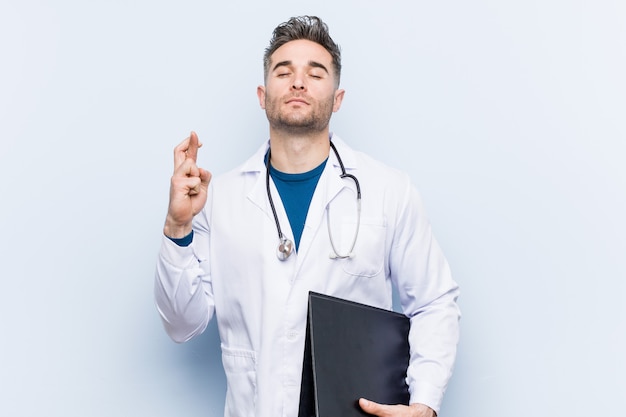 Caucasian doctor man holding a folder crossing fingers for having luck