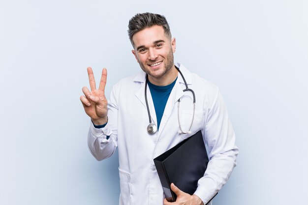 Caucasian doctor man holding a folder showing victory sign and smiling broadly.