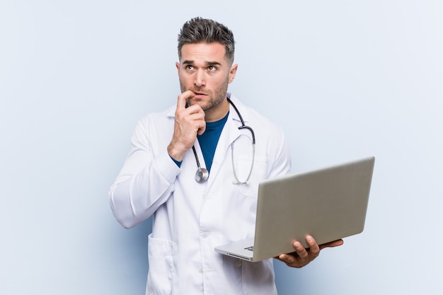 Caucasian doctor man holding a laptop relaxed thinking about something looking at a copy space